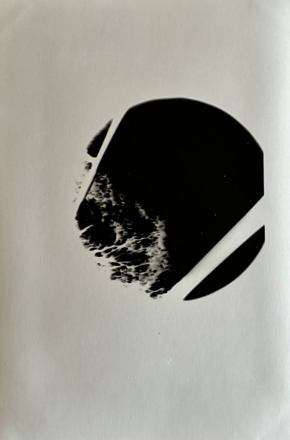 Pinhole photograph: a black disc cut by a pale diagonal, with marbled edges