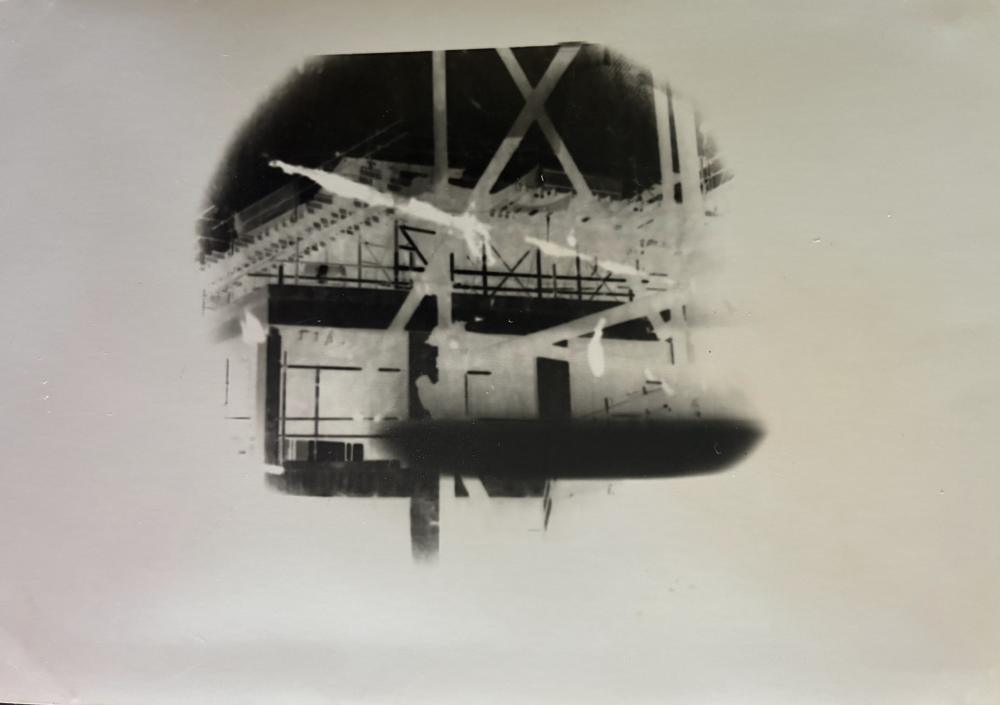 Pinhole photograph: a building’s steel frame and windows inside a round black vignette on a pale ground