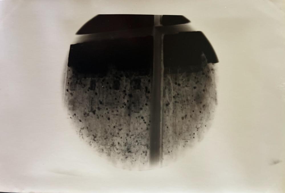 Pinhole photograph: a round view of a dark speckled wall crossed by a vertical post