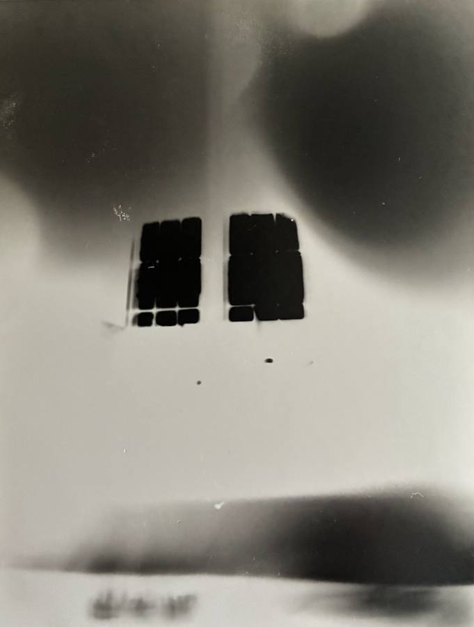 Pinhole photograph: two dark window grids under soft dark shapes, above a blurred horizon