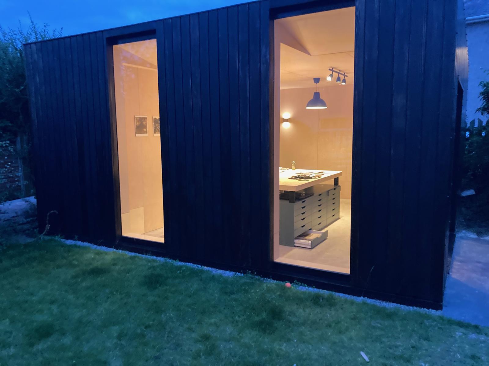The finished studio at dusk, black timber with two lit windows
